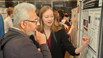 older male faculty member with white hair looking at research poster while female graduate student points and explains