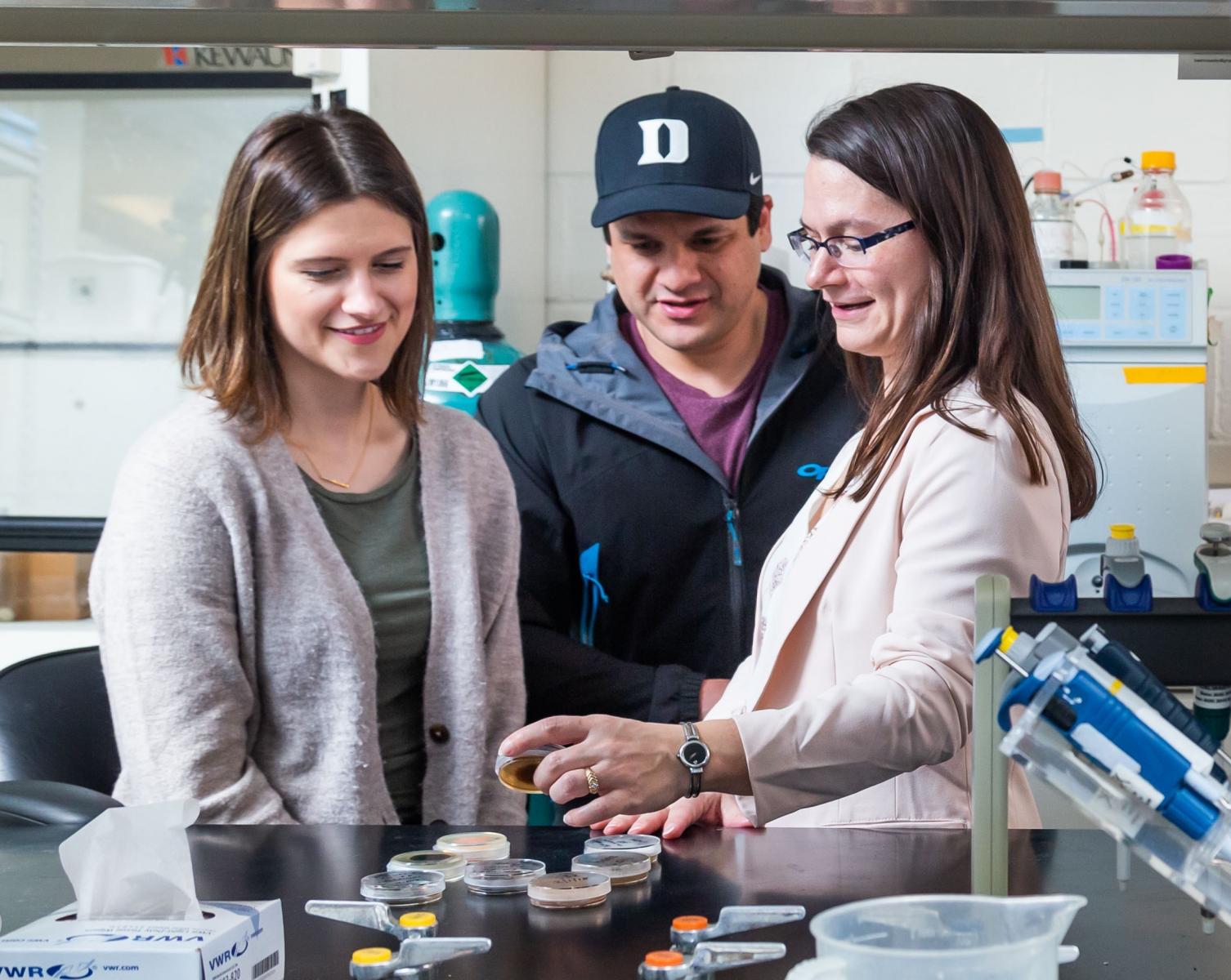 three people in wet lab looking at petri dishes